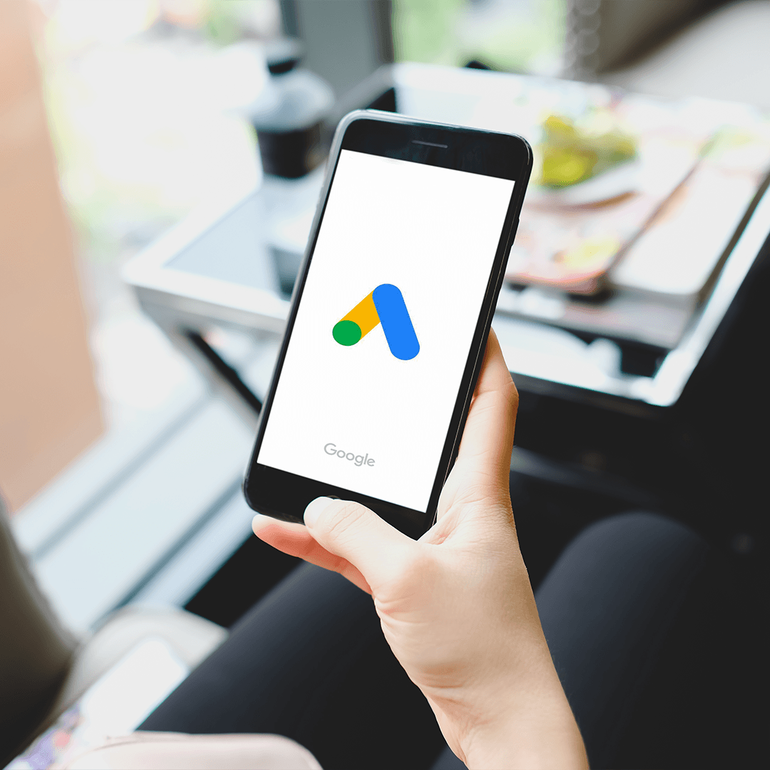 Elde tutulan akıllı telefon ekranında Google Ads uygulaması logosu - Google Ads ve SEO karşılaştırması